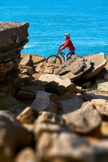 Senior woman riding her electric mountain bike on the rocky cliffs of Peniche at the western