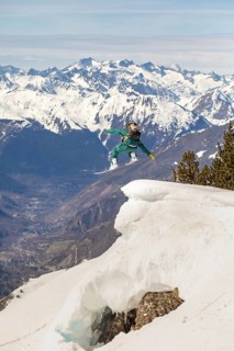 A snowboarder performs an exhilarating jump off a snow-covered ridge, surrounded by majestic