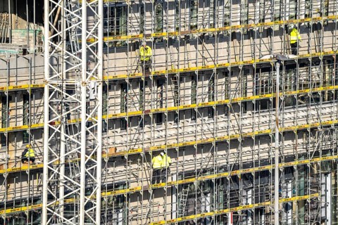Large construction site, scaffolded new building, factory and office building, workers on the