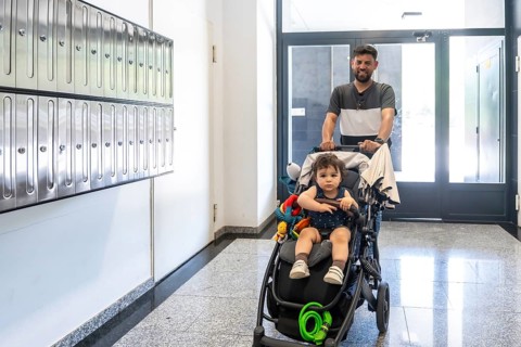 Father returning home, pushing a baby stroller with his young son in a residential building