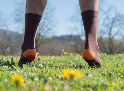 A close-up of a man's feet wearing brown and orange socks as he walks on a meadow surrounded by