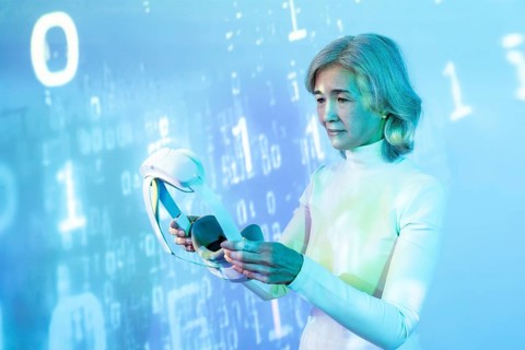 An elderly Asian woman engages with virtual reality technology, represented by a headset, set