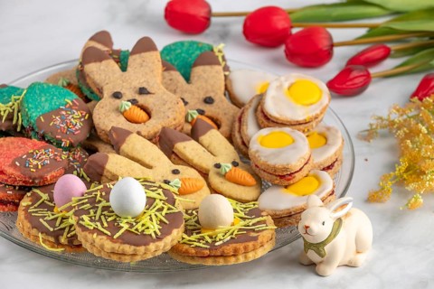 Plate of colourful Easter biscuits, decorated with carrots and eggs, next to red tulips
