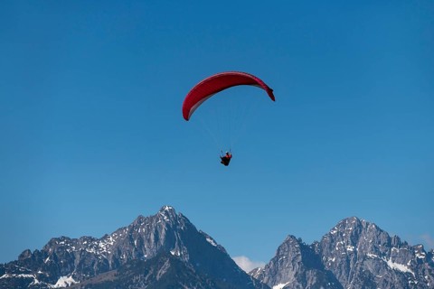 Paraglider with red glider high above snow-covered mountain peaks, Schwangau near Füssen, Ostallgäu