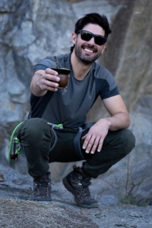 Vertical portrait of a smiling man squatting, wearing sunglasses and hiking gear, enjoys a