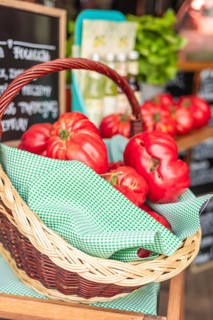 A wicker basket filled with ripe red tomatoes sits on a wooden table. The background features green