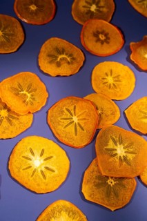 Brightly lit, translucent slices of dried persimmon arranged artistically on a vivid purple