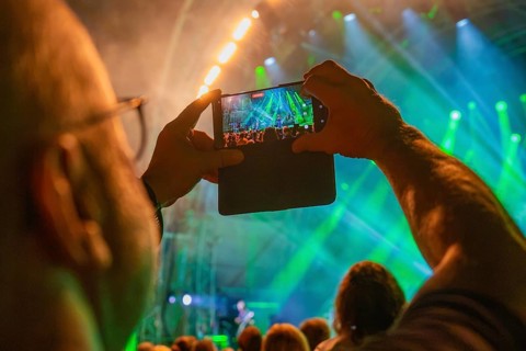 Person holding a smartphone, taking pictures of the concert with green stage lights and a crowd of