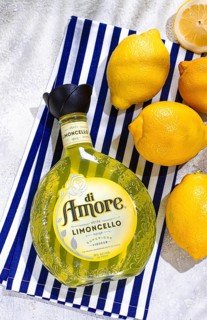 A clear bottle of di Amore limoncello is placed on a blue and white striped cloth. Fresh lemons are