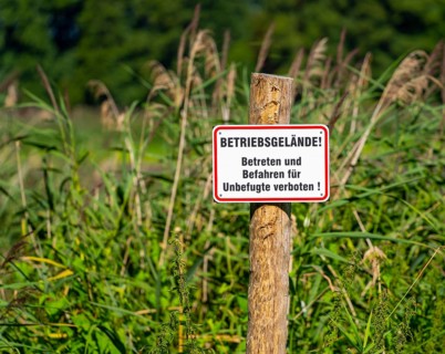 Sign attached to a wooden post surrounded by reeds, company premises, entry prohibited, Heiligsee,