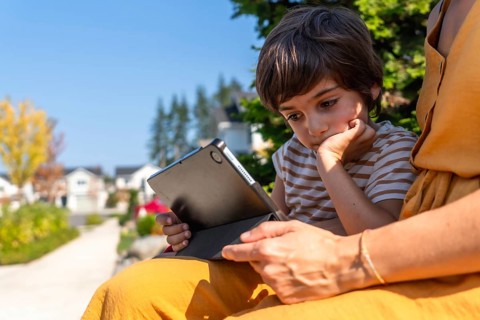 Young boy intently watching and learning on a digital tablet held by a parent, enjoying screen time