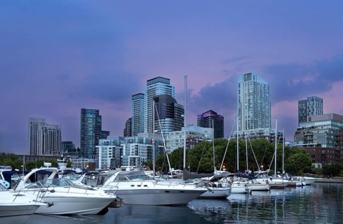 Yachts and sailboats moored at a harbour marina with high rise skyline buildings and skyscrapers