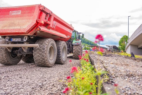 Large construction truck lined with blooming flowers on gravel road, Leonhard Weiß electrification