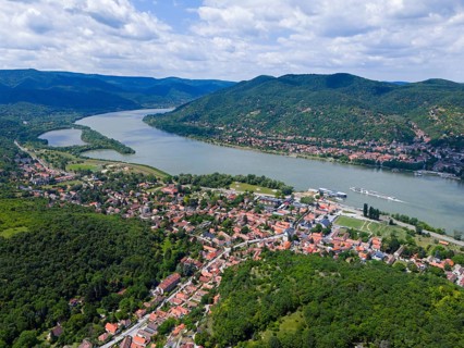 Wide river valley with red tiled roofs, green forests and surrounding mountains, aerial view,