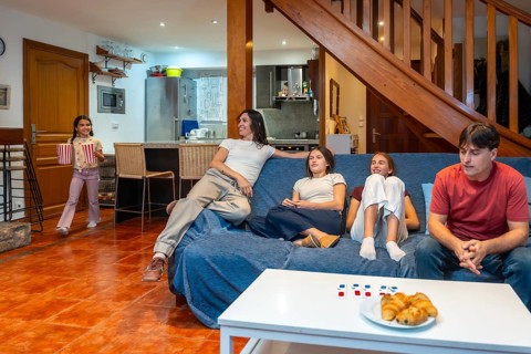 Family relaxing on a blue sofa in a cozy living room, watching tv together while a young girl
