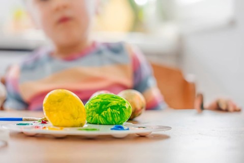 Colorful Easter yellow and green eggs in focus with blurred child in bunny ears background. holiday