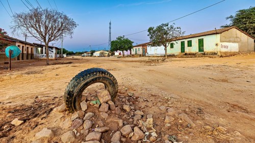 Unpaved road in a village marked by drought, with a tire in the ground as a roadblock under a clear