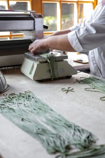 Woman preparing handmade pasta. Woman's hands working with dough to make pasta. Chef making green