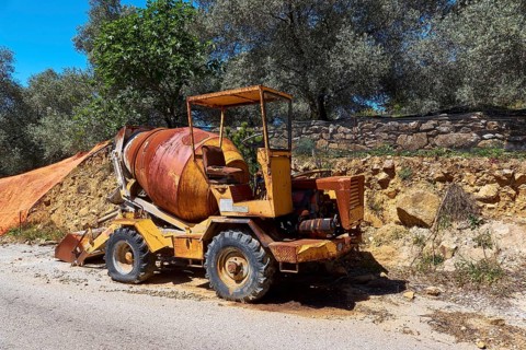 Rusty yellow construction machine with worn appearance by the road in a sunny environment, wrecked