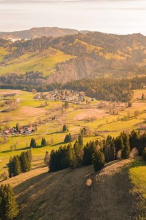A panoramic view of a village between green hills and wooded mountains, Allgäu, Bavaria, Germany