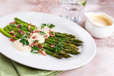 Fresh asparagus with cream sauce and bacon, on a white oval plate, light marble table, sunlight,