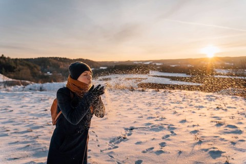 A woman blows in the palm of her hand with snow at sunset in winter