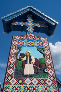 Traditional Sapân?a wooden cross with colorful design and a horse in a rural cemetery, traditional