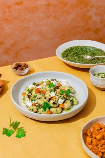 White plate filled with delicious Italian gnocchi mixed with bright green pesto, diced vegetables,