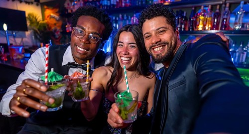 Cheerful multi ethnic friends capturing a joyful selfie while savoring colorful cocktails at a