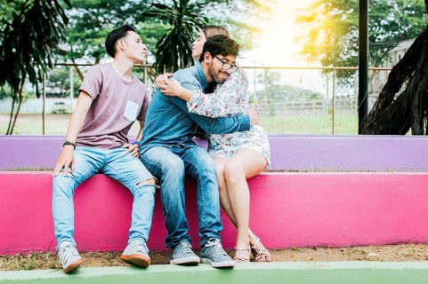 Unfaithful girl sitting hugging her boyfriend and secretly kissing another man. Unfaithful