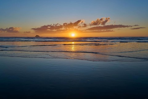 Tranquil coastline at sunrise with gentle waves and warm light, Muriwai Beach, Auckland, North