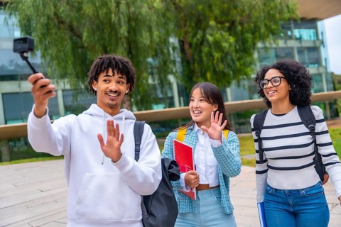 Three multi-ethnic students waving during video call outside the university collage