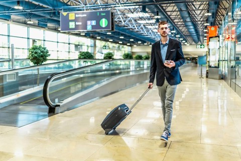 Businessman pulling a suitcase while using a smartphone, walking confidently through a busy airport