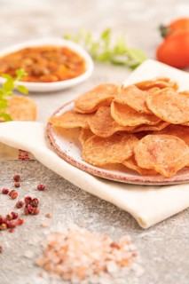 Slices of dehydrated salted meat chips with herbs and spices on gray concrete background and white