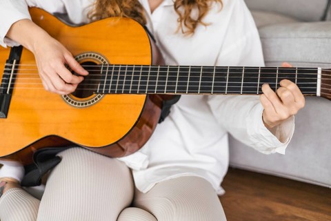 Person playing an acoustic guitar in a relaxed setting with focus on hands and instrument, creating