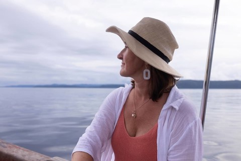 A mature woman tourist wearing a sun hat gazes out over the sea at a homestay on Kri Island, in the