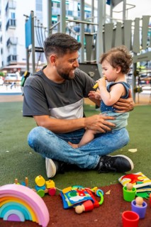 Happy dad sitting criss cross applesauce on the soft ground, embracing his toddler son who is