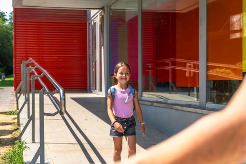 Young girl smiling and walking out of school after class, holding an adult's hand, embodying