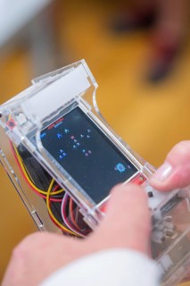 A person holds a transparent handheld console with an arcade game running, Youth Research Center,