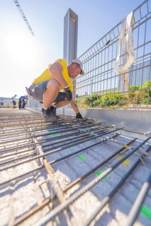 Construction worker in yellow T-shirt working on metal reinforcements on a construction site in