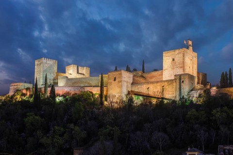 Night view of the historic Alcazaba at the Alhambra illuminated against a dramatic twilight sky,