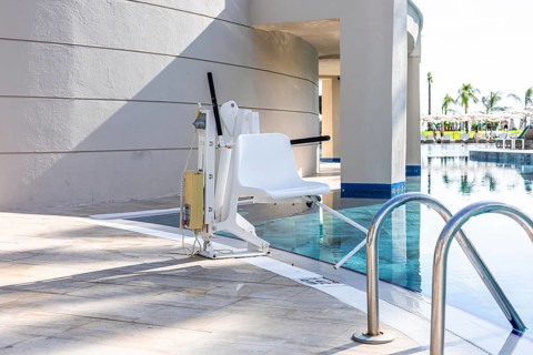 A poolside lift chair for disability people is positioned next to a swimming pool. The area is