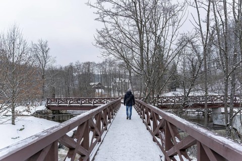 A man crosses the river in winter on a wooden bridge, A person walks alone on a snow-covered wooden