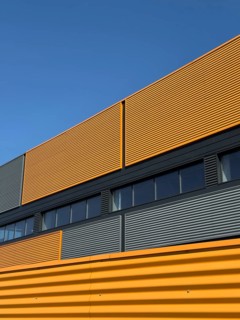 A contemporary industrial building exterior featuring a vibrant yellow and grey facade under a