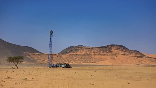 Desert landscape with wind turbine, off-road vehicle and tree under a clear blue sky, water pump in