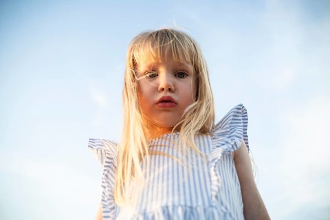 A young girl gazes into the camera with a thoughtful expression as the golden sunlight highlights