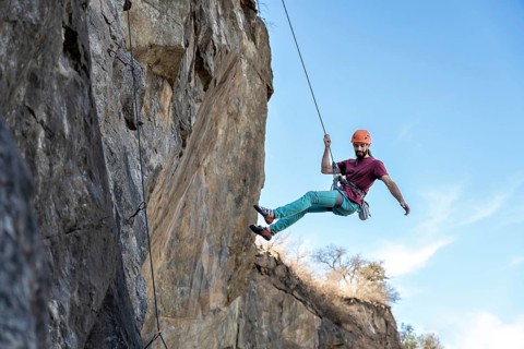 A determined young man ascends a steep cliff, using a rope for support, highlighting his strength