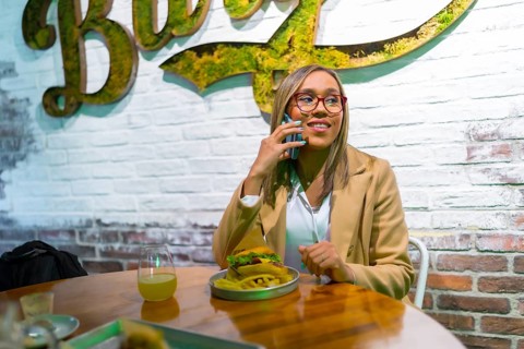 Latin woman talking to the mobile while eating burger in a modern fast food restaurant