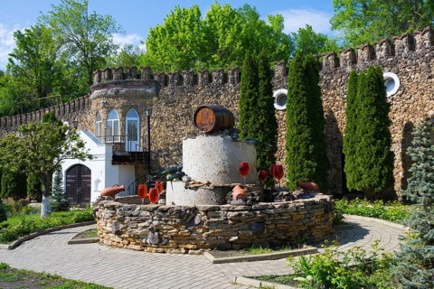 Garden with barrel in front of an arched stone wall surrounded by green cypresses, fountain with