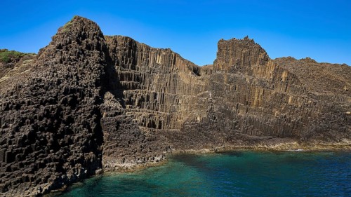 Wide rock wall with geological patterns merging into the sea, Glaronisia, Glaronesia, Milos,